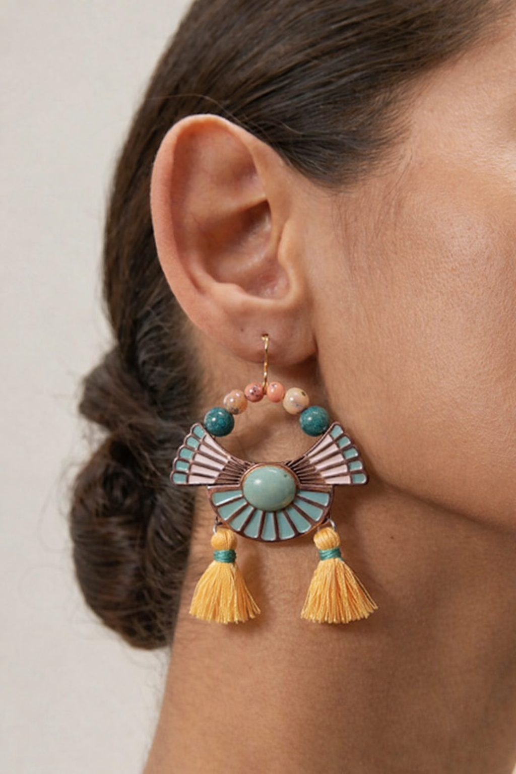 Art Deco-inspired statement earring — teal enamel fan, stone beads, and yellow tassels, worn close-up